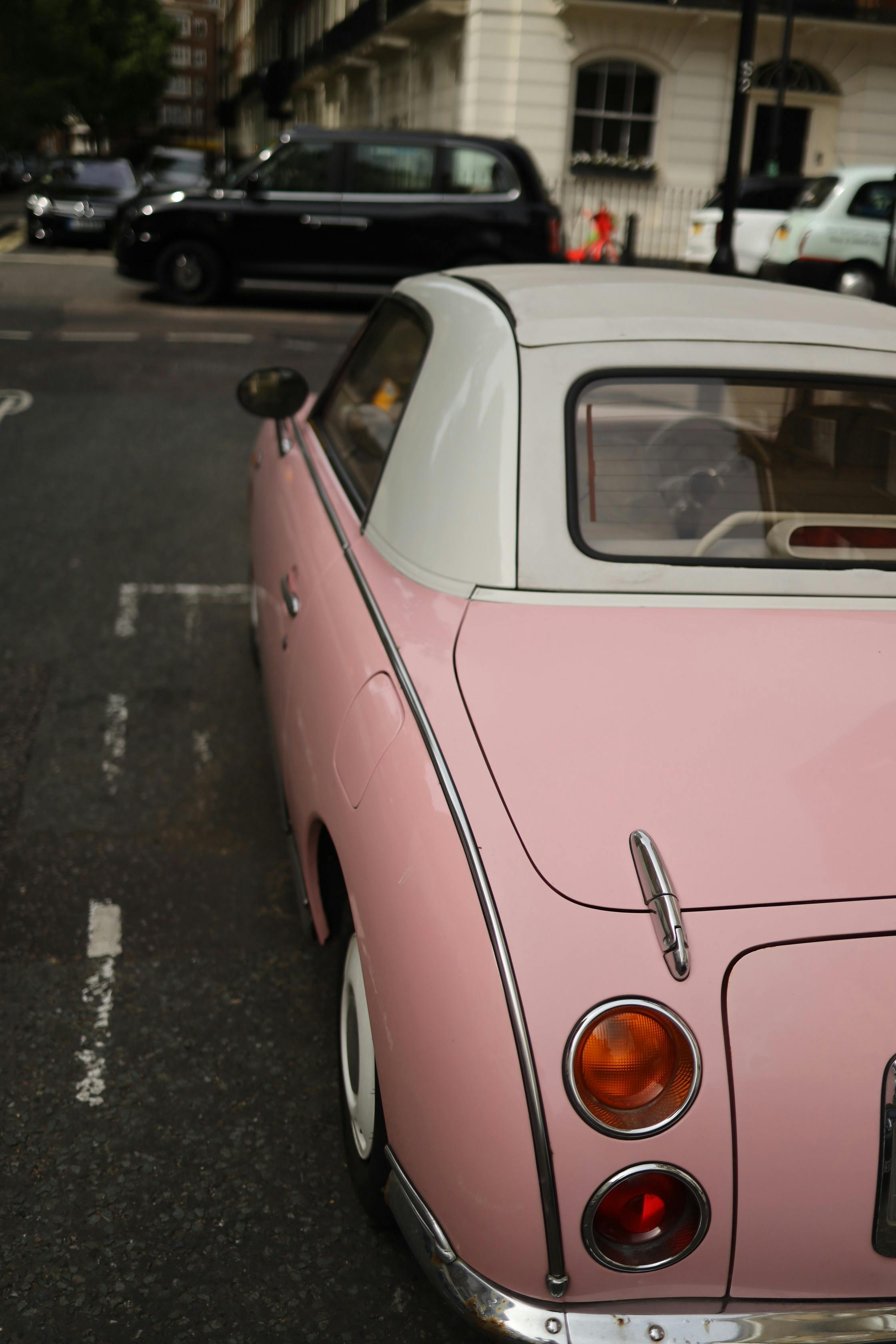 A vintage pink car with a white roof parked on an urban street corner, showcasing classic automotive style.