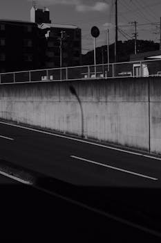 Black and white urban scene featuring shadows on a concrete wall by an empty street.