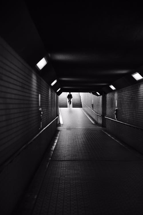 Grayscale Photo of a Man Riding a Bicycle on an Underpass