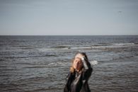 Woman in Leather Jacket Fixing Her Hair while Standing on the Sea Shore