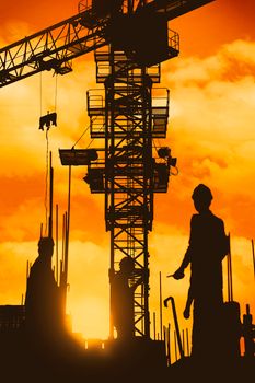 Silhouetted construction workers with a crane at sunset, creating a striking industrial scene.
