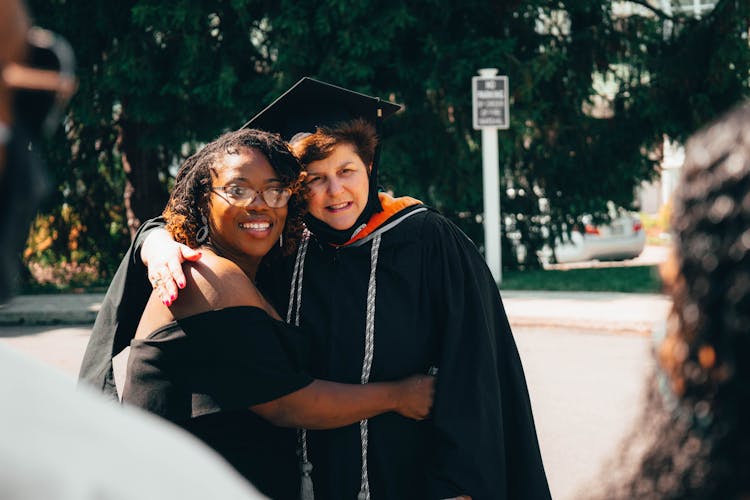 Women In Academic Dresses Hugging During Graduation 