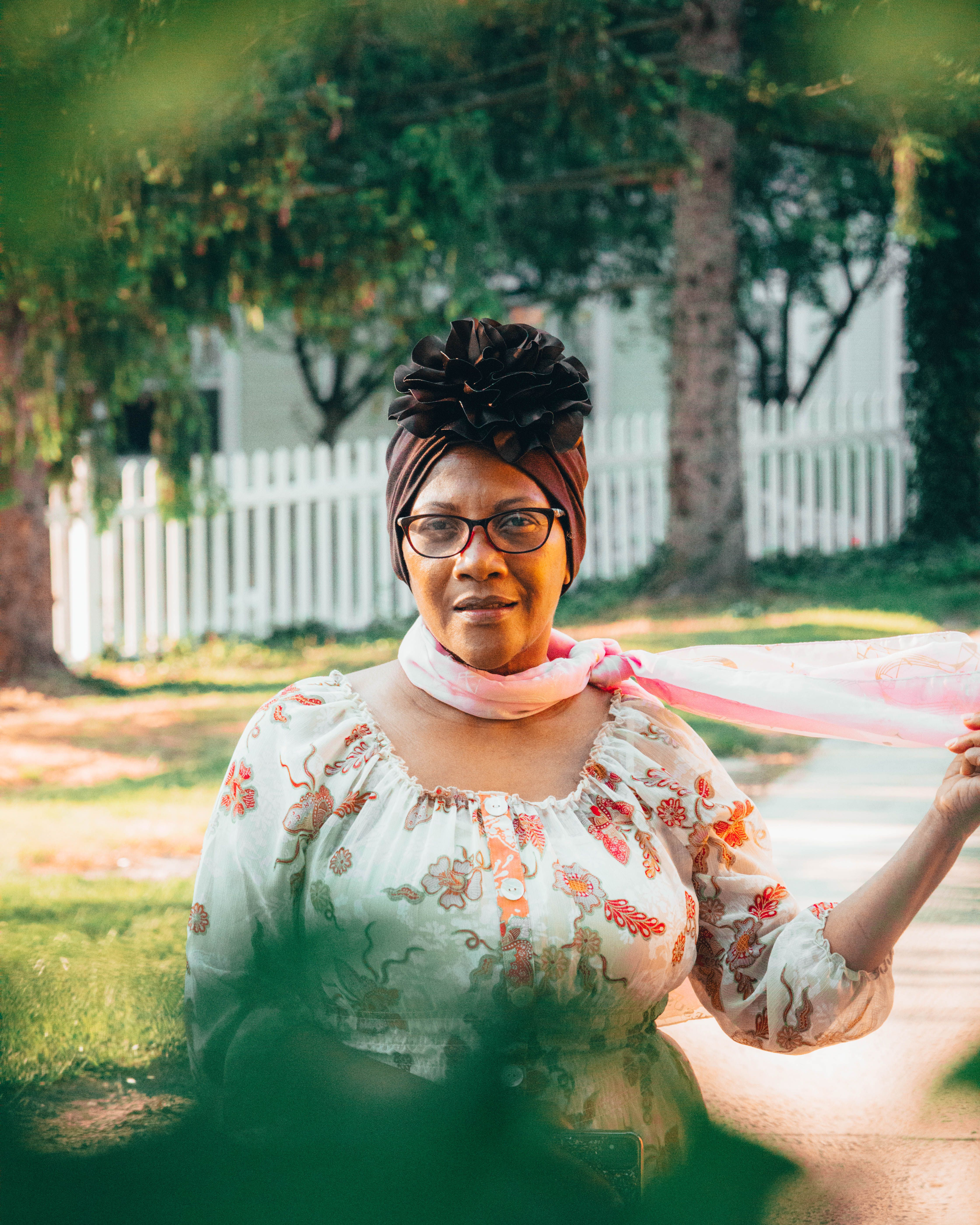 Woman with glasses and headscarf in a peaceful garden, showcasing leisure and grace.