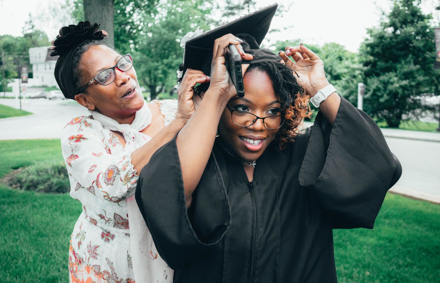 A touching moment as a mother helps her daughter with her graduation cap outdoors.