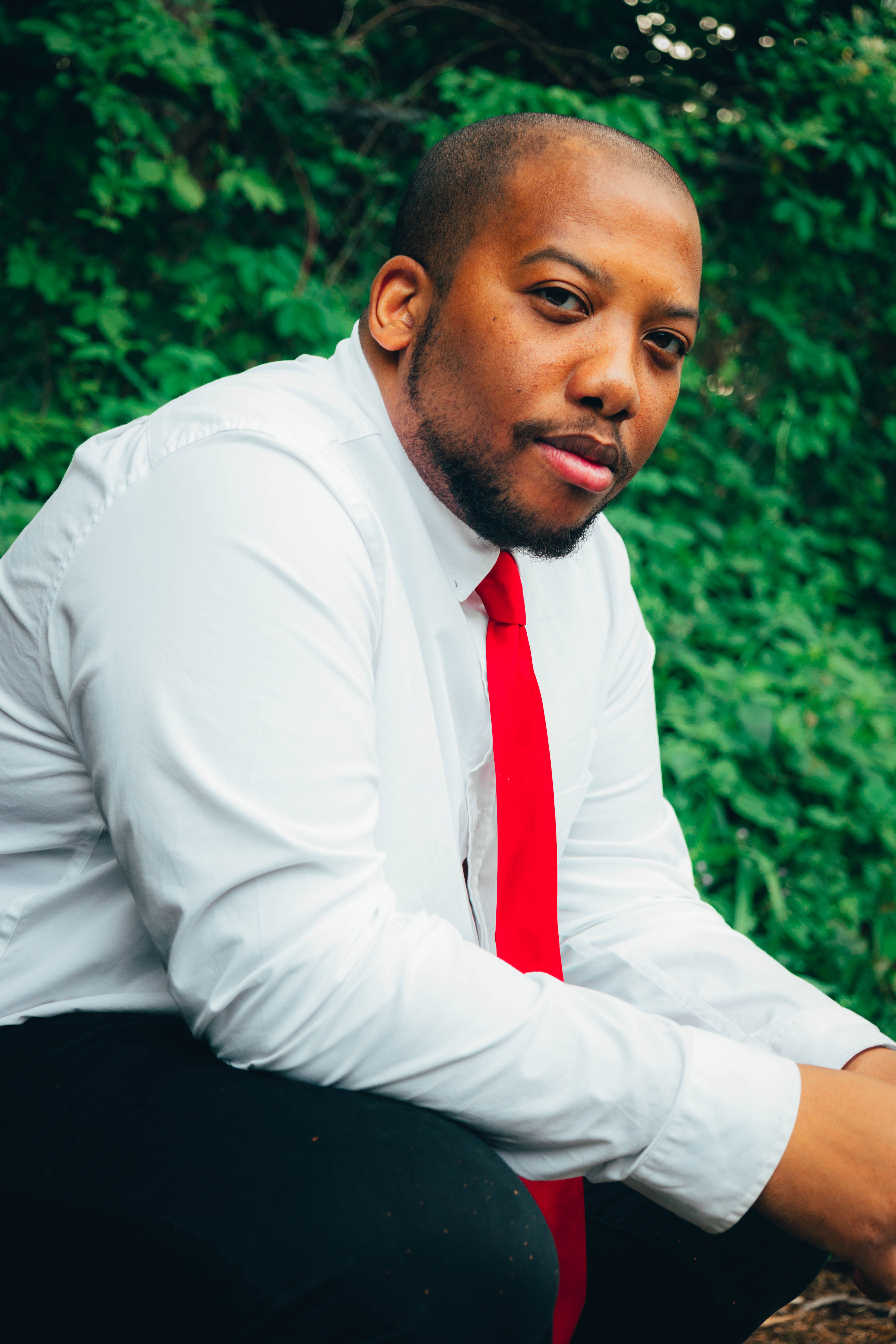 Portrait of a confident man in a white shirt and red tie sitting outdoors on a sunny day.