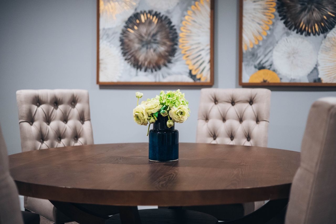 Dark wood round dining table with a floral centrepiece and tufted chairs