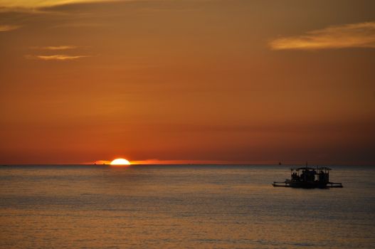 A tranquil sunset over the ocean with a solitary silhouette of a boat creates a peaceful scene.
