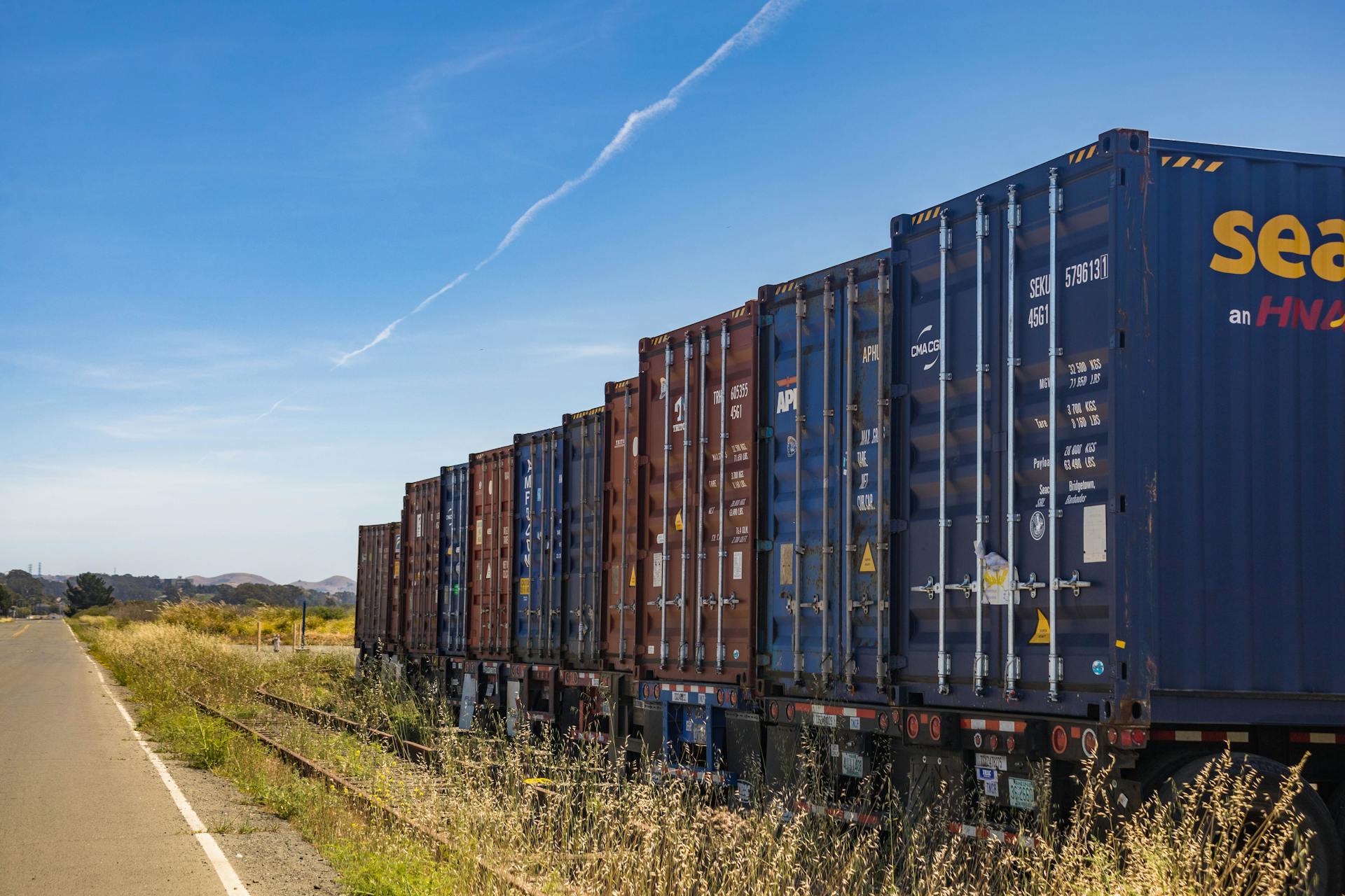 Colorful cargo containers on a freight train along a rural railway track under a clear blue sky.