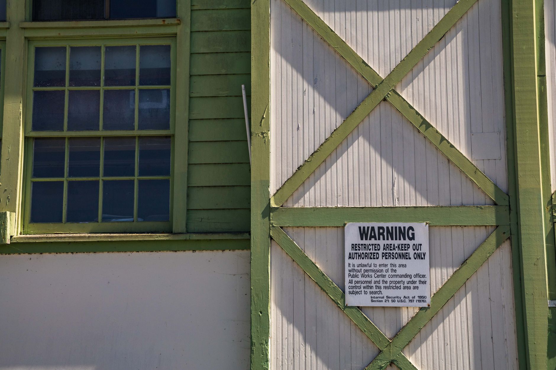 Close-up of a vintage building featuring a warning sign and green trim, emphasizing restricted access.