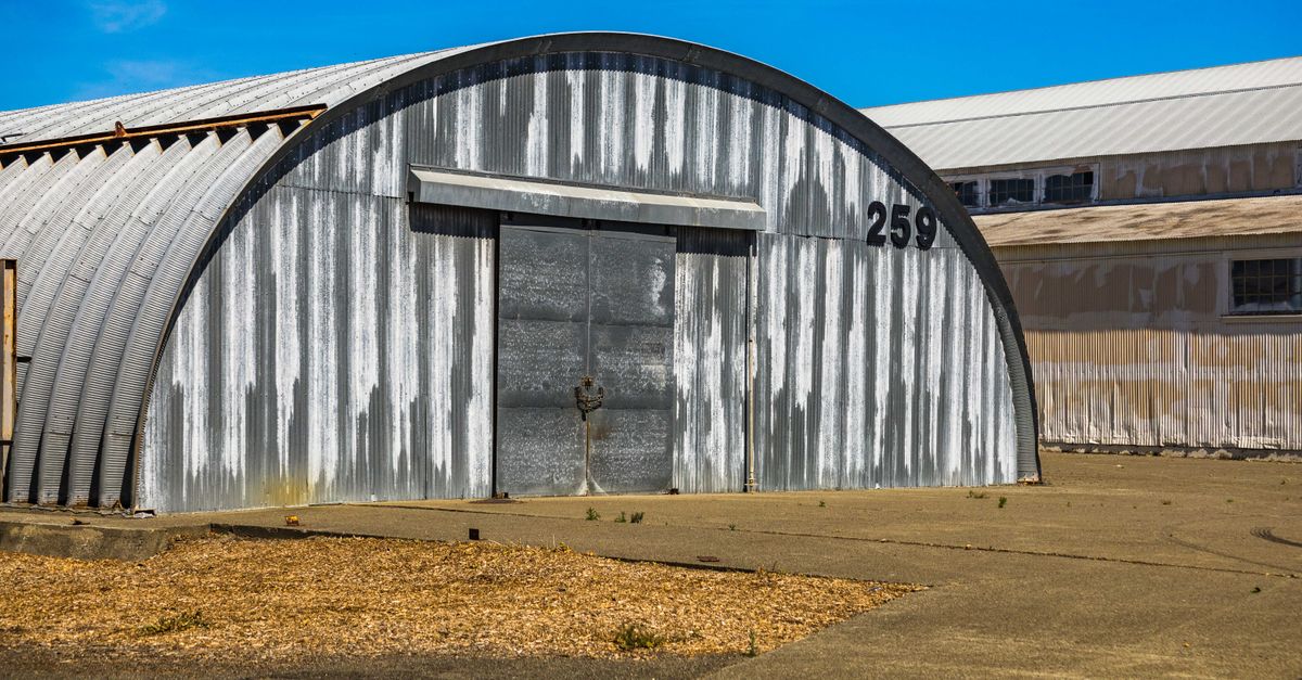 An aged metal warehouse with a curved roof and number 259, showcasing an industrial rustic design.