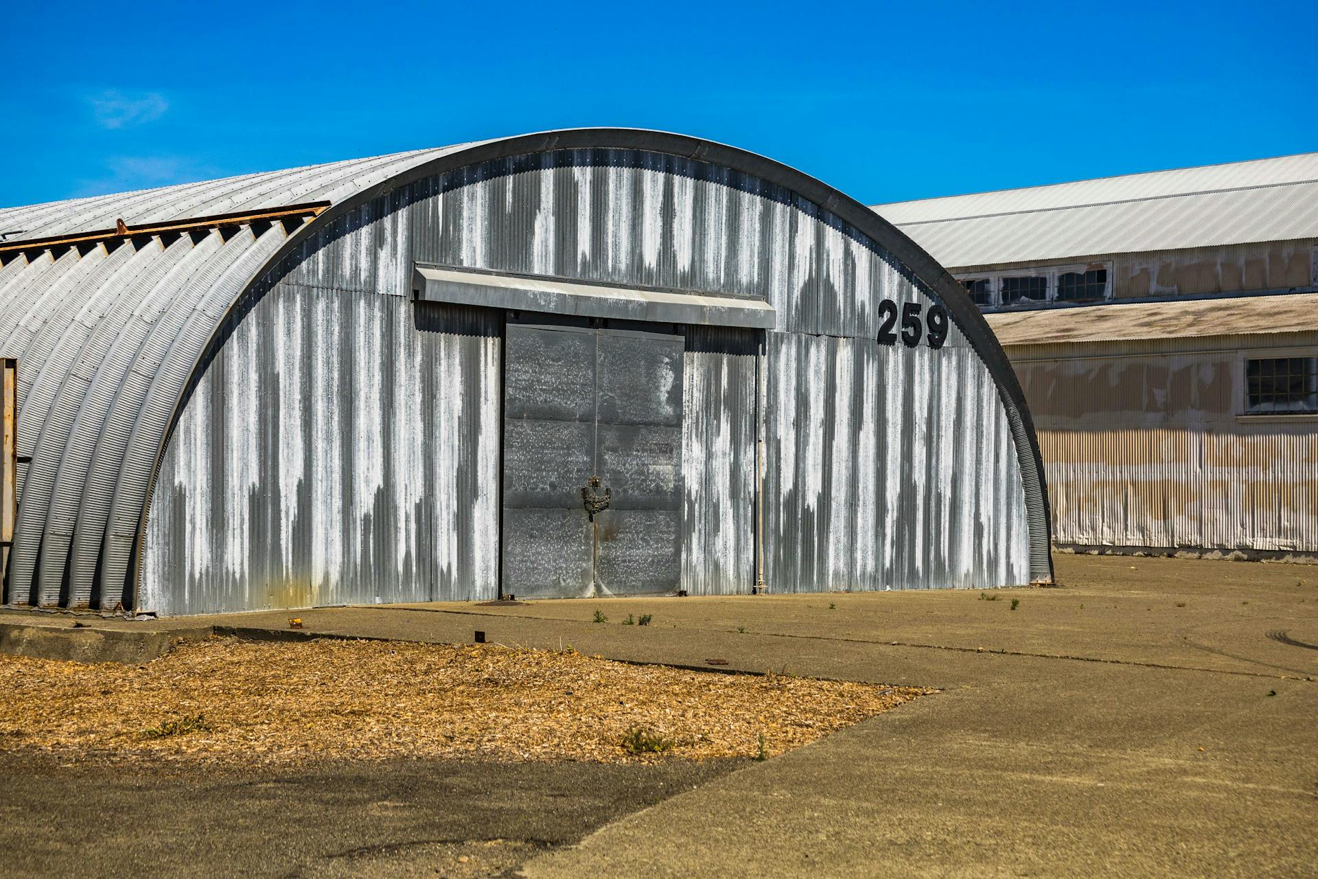 An aged metal warehouse with a curved roof and number 259, showcasing an industrial rustic design.