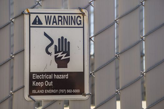 Close-up of a warning sign for electrical hazards on a chain-link fence.