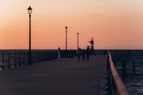 People Walking on Gray Concrete Dock During Sunset