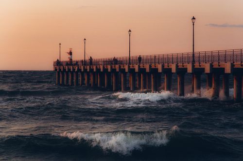 Free A picturesque pier extends into the ocean during a dramatic sunset, with waves crashing around. Stock Photo