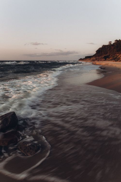 Free Peaceful beach shoreline during sunset with gentle waves and rocky coast. Stock Photo
