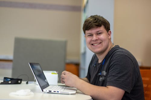 Smiling Man Sitting at Table Working on Laptop