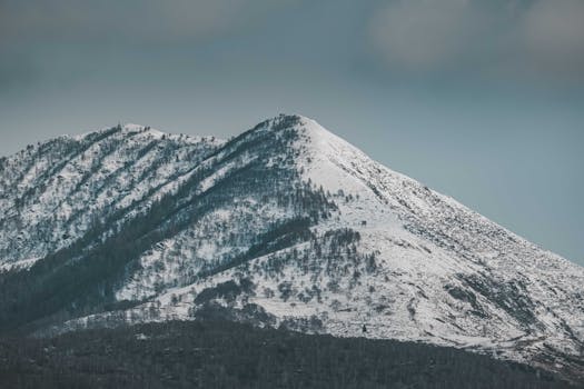A snow-covered mountain peak with a cloudy sky, captured in a serene winter landscape.