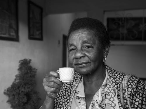 Grayscale Photo of an Elderly Woman Holding a White Tea Cup