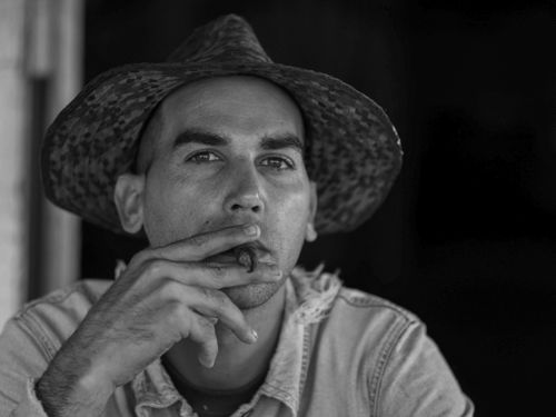 Free Monochrome portrait of a man wearing a cowboy hat, smoking a cigar. Intense gaze. Stock Photo