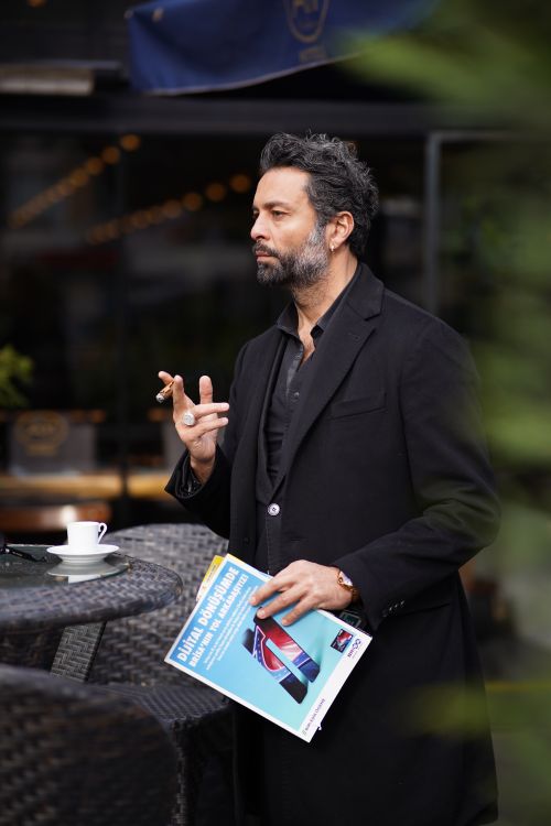 Free Fashionable man with facial hair smoking outside a café, holding a vibrant magazine. Stock Photo