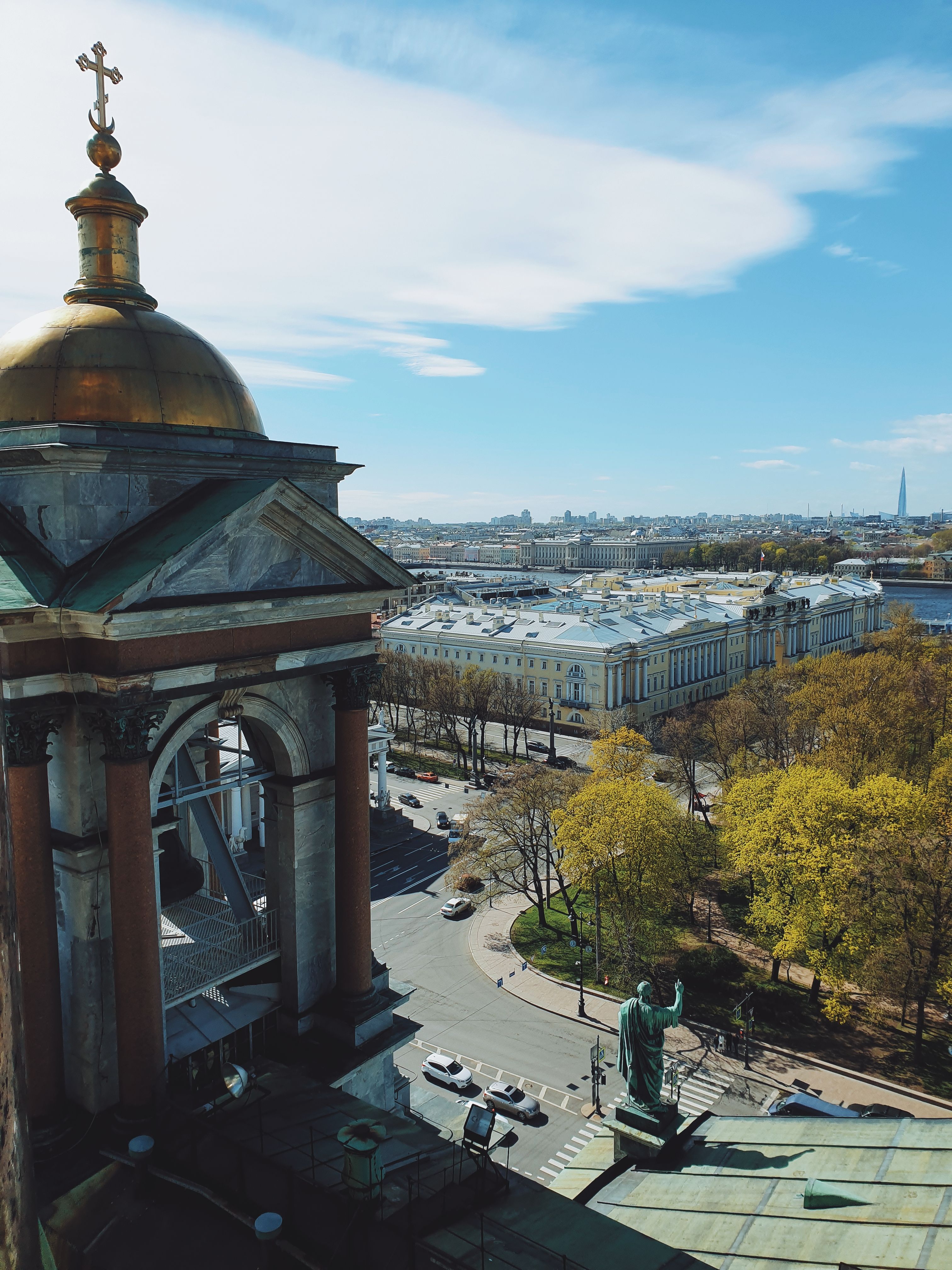 A stunning view over the city skyline from St. Isaac's Cathedral, capturing urban architecture and lush greenery under a blue sky.