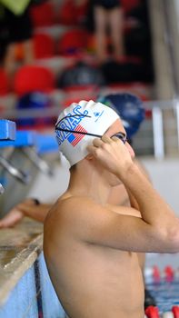 Young male swimmer adjusting goggles poolside in Istanbul, focused on upcoming race. — photo by Yaggy Gurtug