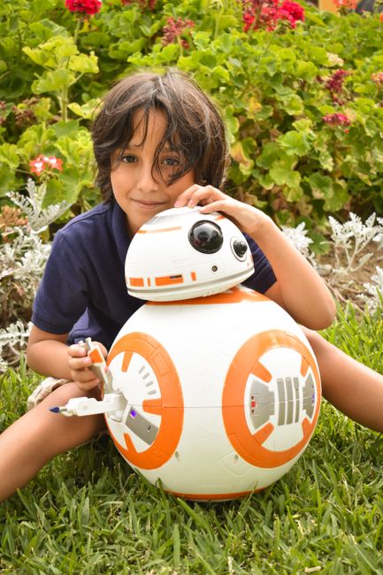 Fotomural Niño pequeño disfruta de un momento juguetón con un juguete robot en un jardín, Lima, Perú.