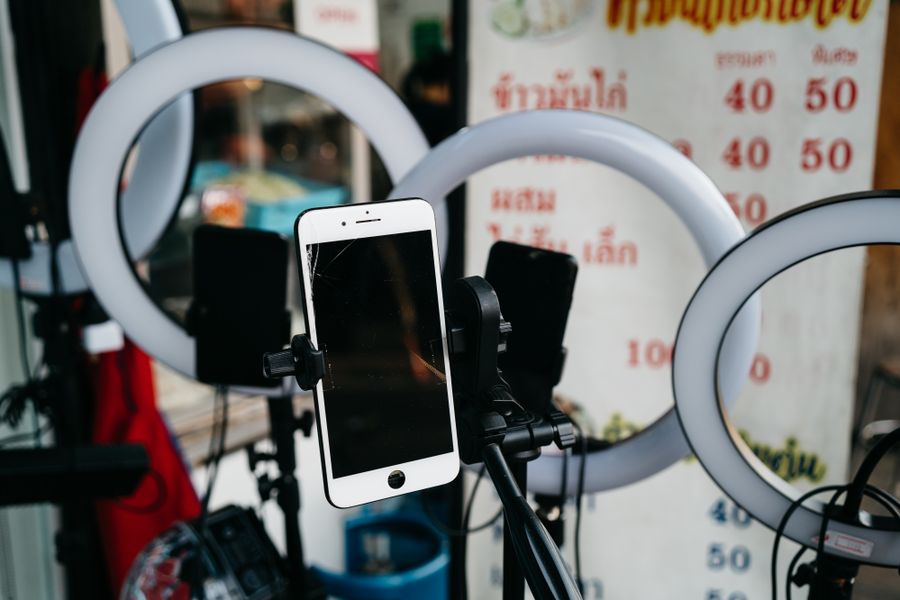A smartphone mounted on a tripod ringed by lights, set up for a live stream