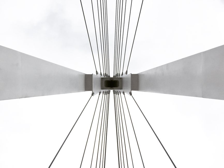 Artistic perspective of a suspension bridge tower and cables against a clear sky.