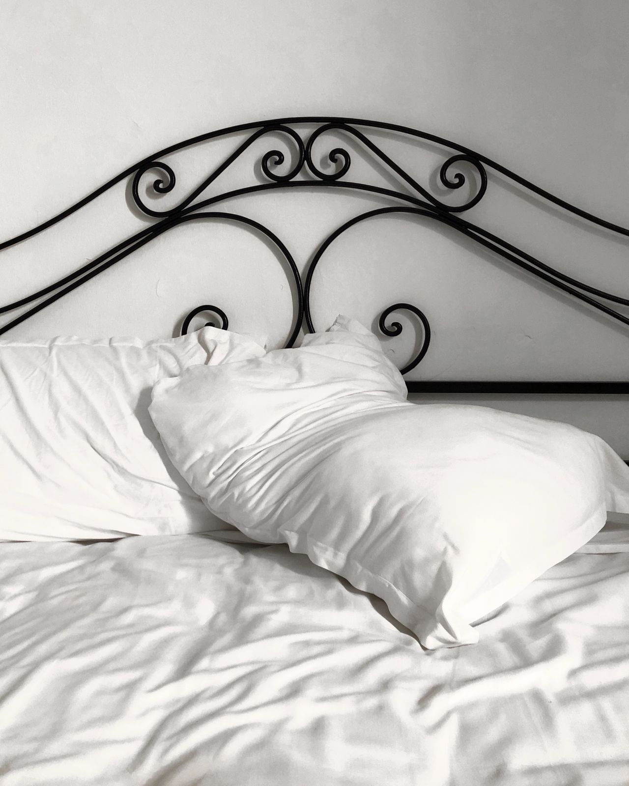 Close-up of a black wrought-iron headboard with scrollwork and white pillows