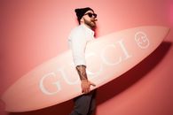Man Holding a Gucci Surfboard and a Cigar in His Mouth