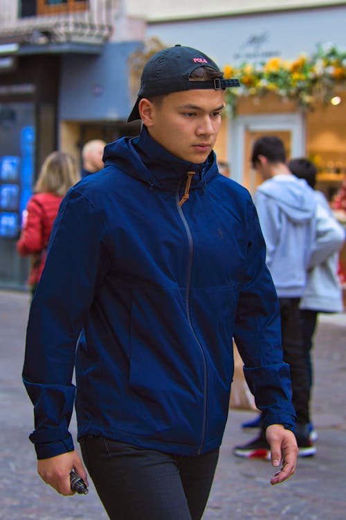 Man in Blue Zip Up Jacket walking on a Street 