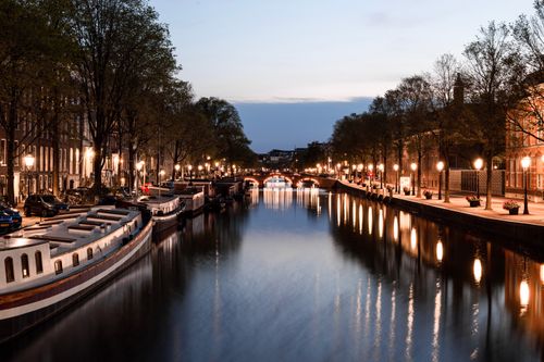 Free Peaceful evening scene of a water canal in Amsterdam with illuminated streets and boats. Stock Photo
