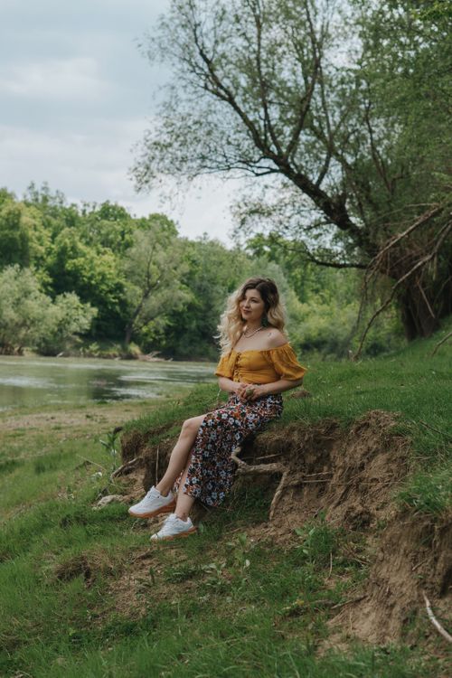 Free Young woman in summer attire enjoying the serene riverbank surrounded by lush greenery. Stock Photo