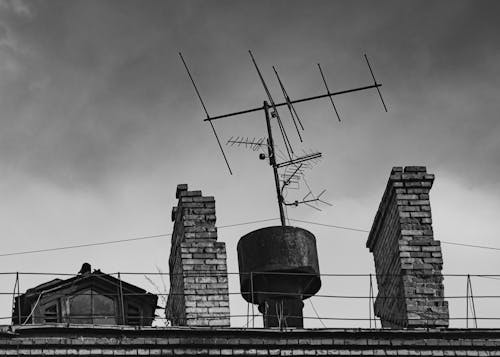 Grayscale Photo of Chimneys and Antenna on a Roof