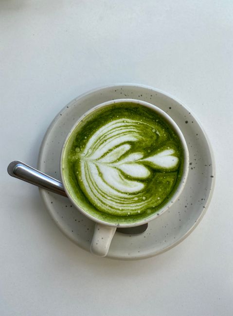 Elegant matcha latte with intricate latte art served in white cup and saucer.