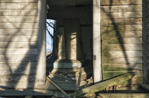 Free A derelict wooden house with a broken doorway, showing decay and wear. Stock Photo