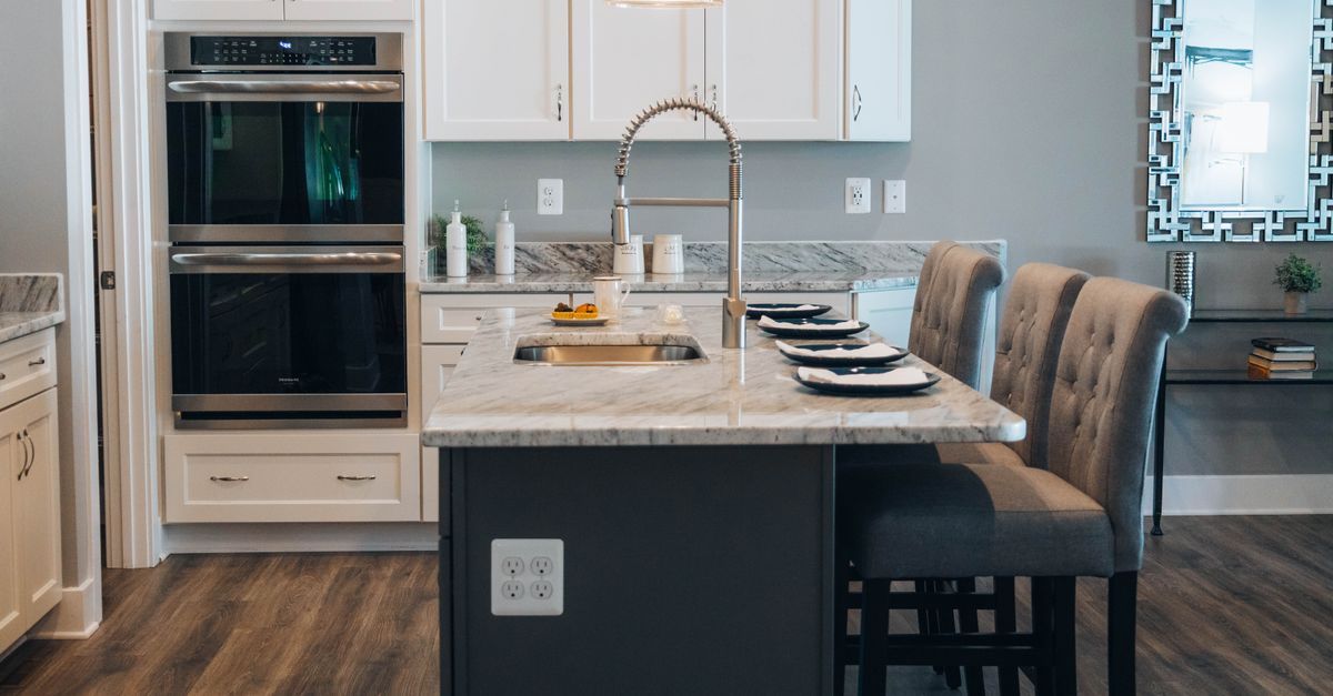 Transitional kitchen featuring a dark grey island, marble countertops, and grey tufted bar stools.