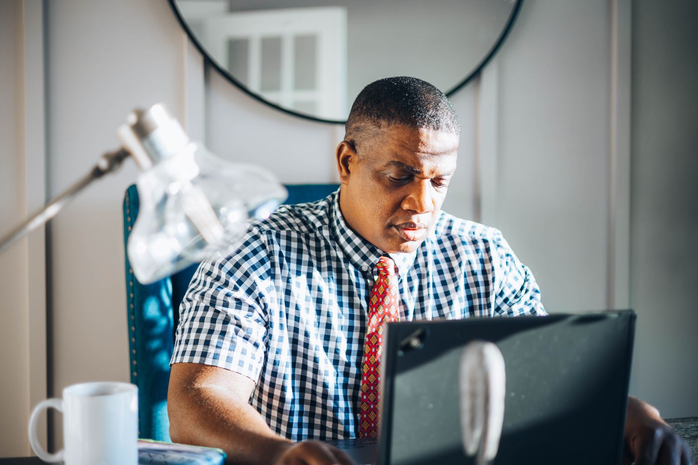 A concentrated adult man working on his laptop in a bright modern office setting.