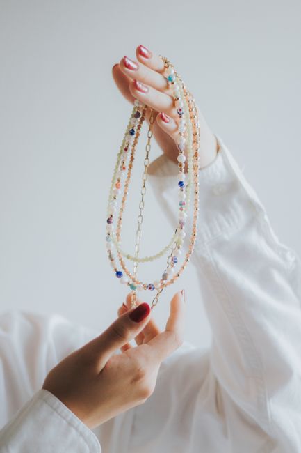 Close-up of hands with red polished nails holding a colorful necklace in a minimalist style.
