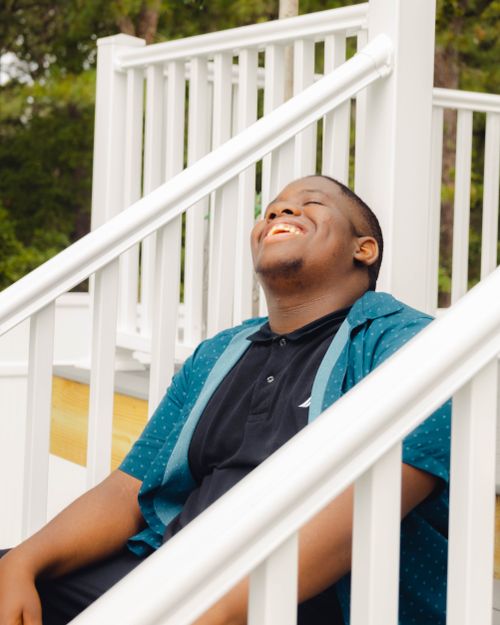 Free Smiling man enjoying a sunny day sitting on outdoor stairs, exuding happiness and relaxation. Stock Photo
