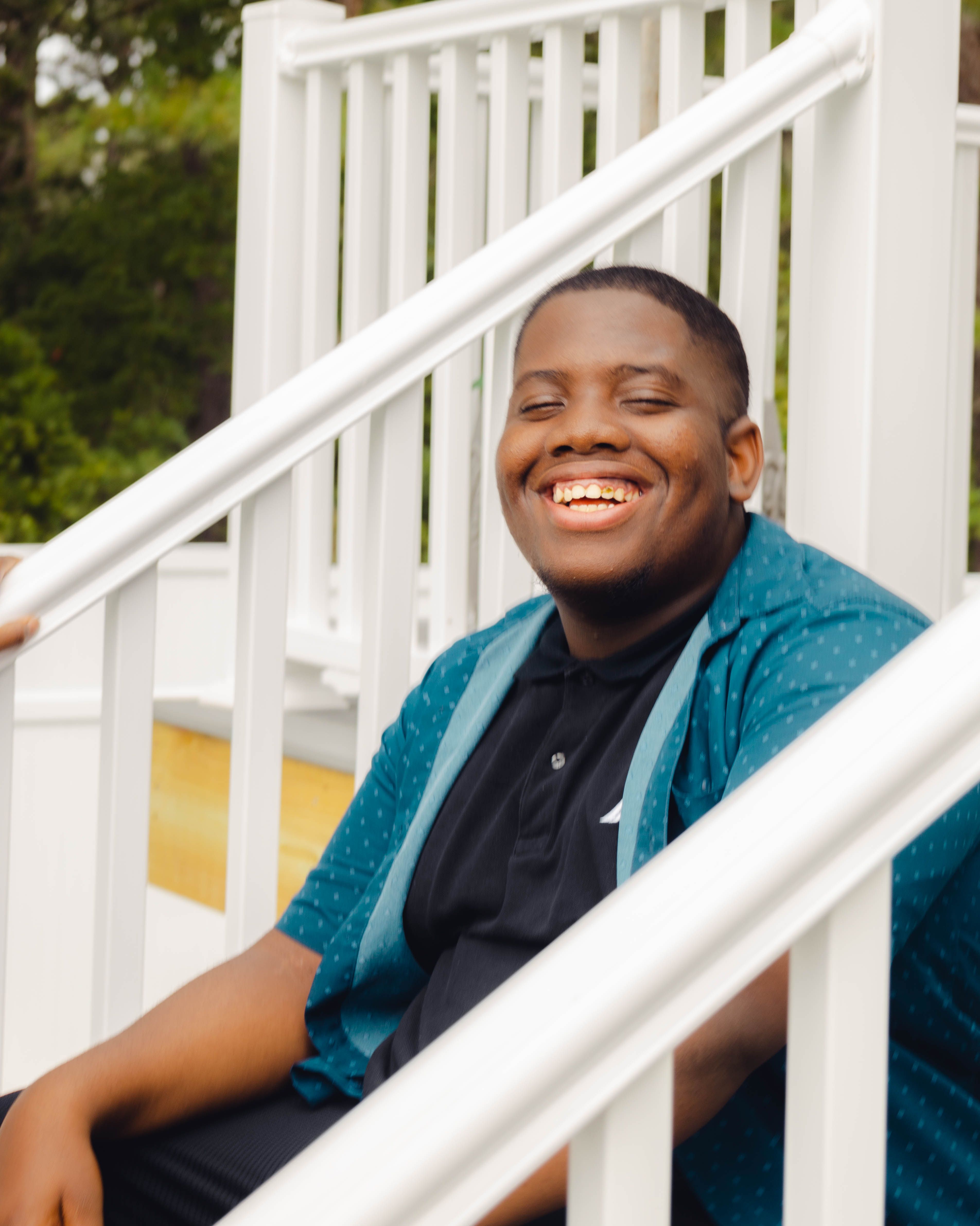 Joyful teenager sitting outdoors on white stairs, smiling brightly.
