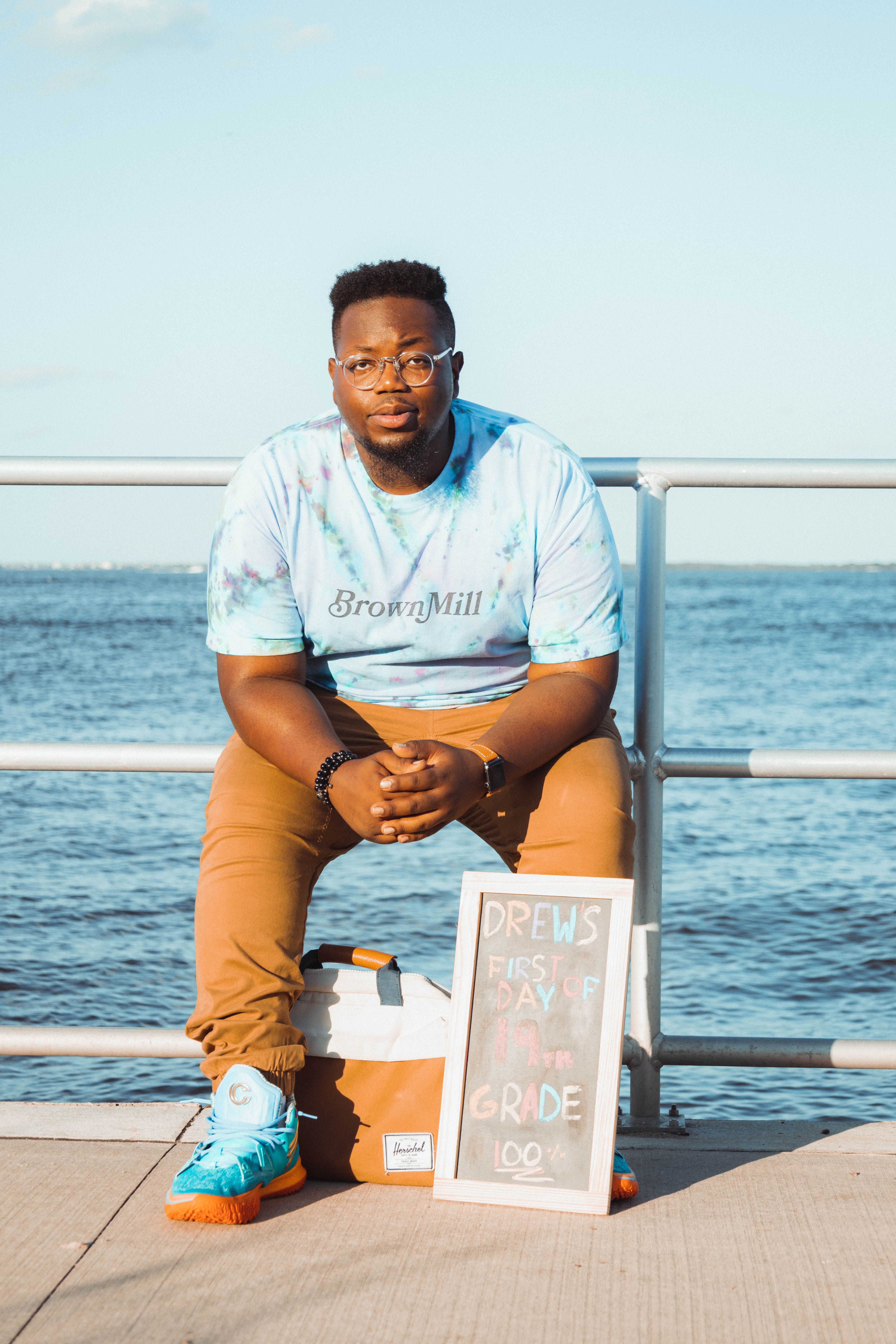 A man in casual attire sitting by the waterfront with a sign, enjoying the sunny day.