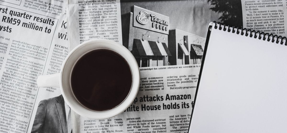 A newspaper, coffee and pen laid out for a morning crossword