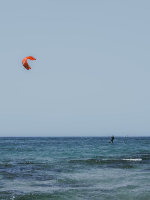 Free Dynamic kite surfer gliding over the ocean on a sunny day, showcasing water sports excitement. Stock Photo