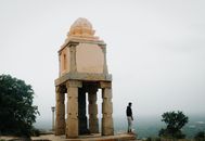 A man stands beside a historic stone pavilion on a foggy day, evoking a sense of solitude.