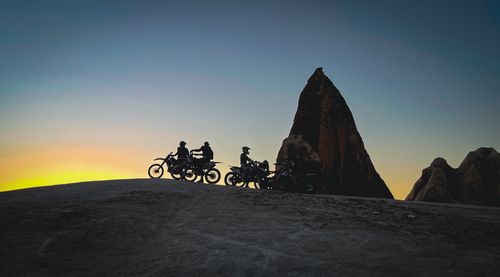 Free Silhouette of motorcyclists paused against dramatic rock formations at sunset, capturing a sense of adventure. Stock Photo