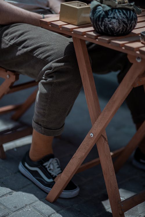 Person in Gray Corduroy Pants Sitting on Wooden Folding Chair 