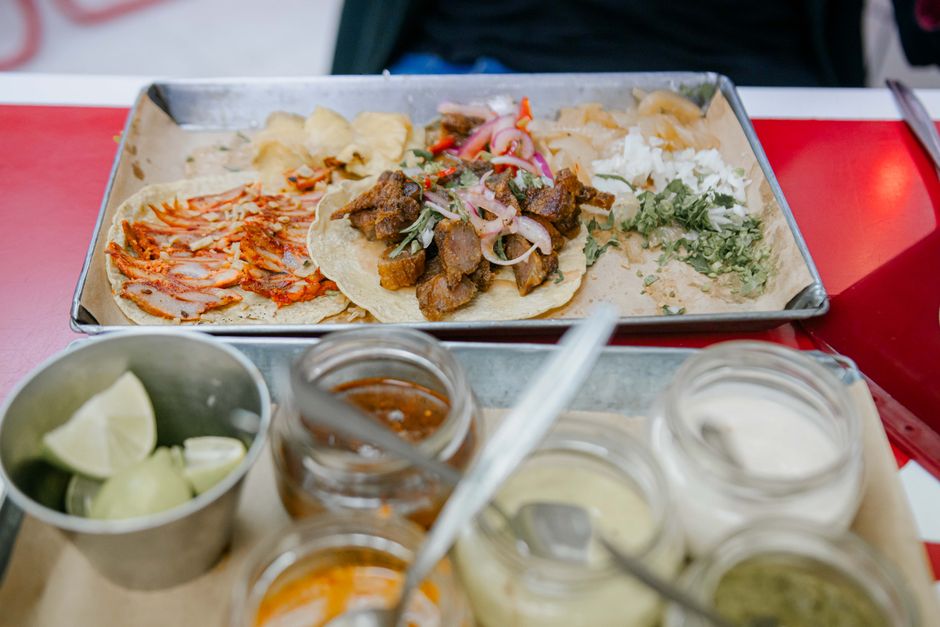 Close-up of a taco platter with lime wedges, assorted sauces, and toppings in a vibrant setting.