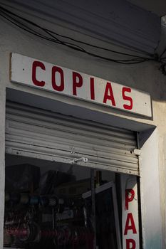 Close-up of a storefront with 'Copias' sign and a partially open metal shutter.